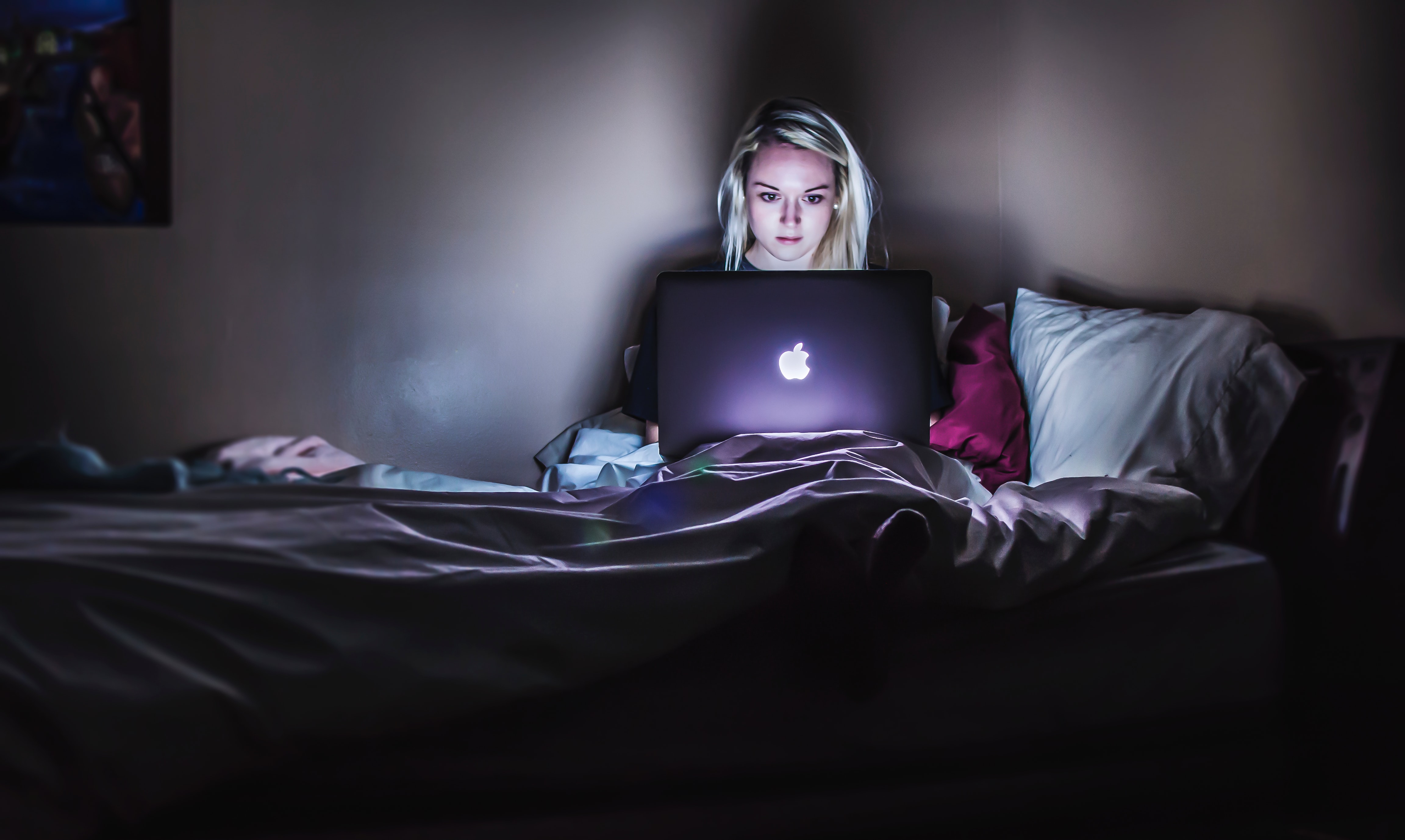 Kobieta ucząca z laptopa się w łóżku.